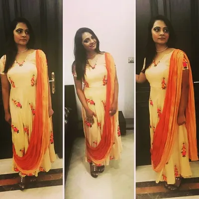 A client looking lovely in a custom-designed floral Anarkali. The light peach fabric is complemented by a contrasting orange dupatta, making it a graceful and comfortable choice for a daytime event.