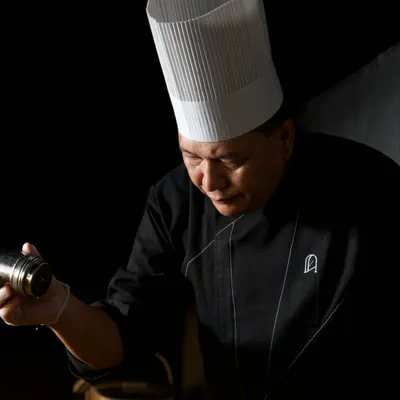 Sharp instincts and sharp skills. Our head chef is captured in a moment of intense focus, adding the final seasoning to a dish before it leaves the kitchen.