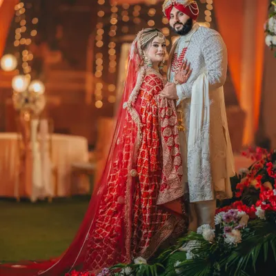 Gurneet and Gurbani in a classic Sikh wedding portrait. The bride's red dupatta and the groom's white sherwani create a stunning contrast against the warm, festive lights.