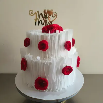 A beautiful two-tier wedding reception cake with a modern wafer paper ruffle design and vibrant red roses. The "Mr & Mrs" topper adds the perfect finishing touch.