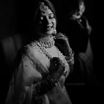 An artistic black and white bridal portrait, using dramatic low-key lighting to highlight the bride's jewelry and serene expression.