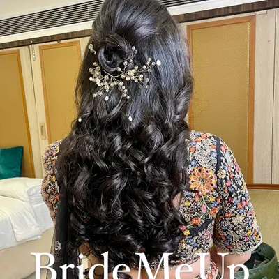 A beautiful half-up, half-down hairstyle for a reception. This style features a delicate rose made of hair and a sparkling accessory, with the rest of the hair in soft, bouncy curls.
