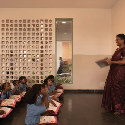 A classroom at the Talaricheruvu Rural School, where students sit on the floor in a traditional manner. The custom-designed jaali wall allows for cross-ventilation and fills the learning space with balanced, natural light.