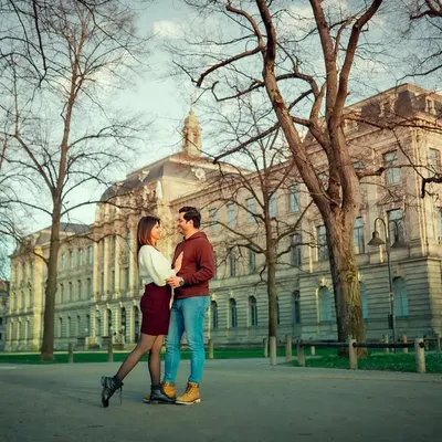 A wide shot of a couple sharing a moment in a European park, with grand architecture in the background. This photo captures the scale and romance of a destination photoshoot.