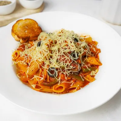 A plate of penne arrabbiata pasta in a rich red sauce, generously topped with shredded cheese and black olives, served with a side of garlic toast. The bright white plate and background make the colors of this Italian dish stand out.