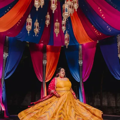 A bride twirls in her vibrant yellow lehenga during her Sangeet, set against a spectacular Moroccan-themed backdrop with colorful drapes and hanging lanterns. This is how I bring a theme to life with energy and style.
