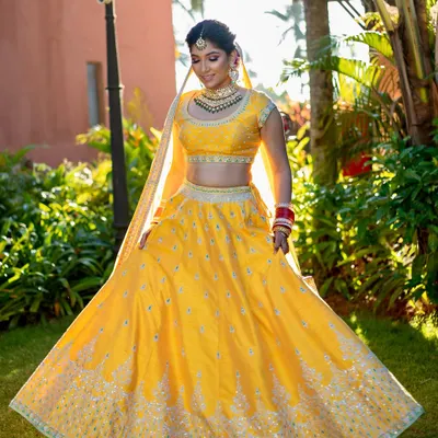 A radiant bride in a sunlit garden. Her makeup is fresh and minimal, with a focus on glowing skin and a soft smile, perfectly complementing her yellow Anita Dongre lehenga.
