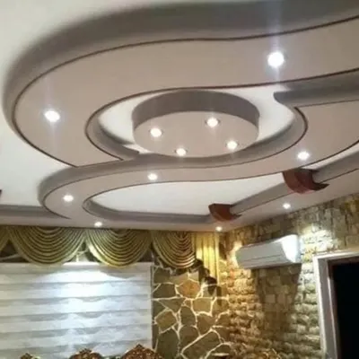 A finished gypsum false ceiling featuring a smooth, curved design with perfectly placed recessed spotlights. This type of design adds a soft, modern flow to a living or dining area.