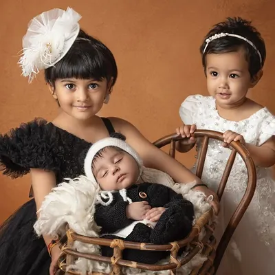 A perfect portrait of sibling love. Two older sisters gently watch over their newborn brother, who is nestled comfortably in a basket.
