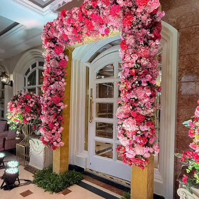 A magnificent floral arch made entirely of pink and red blooms frames a doorway, creating a stunning and romantic entrance for a Roka ceremony.