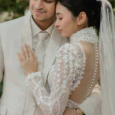A tender moment between the bride and groom, showcasing the intricate details of the bride's high-neck, pearl-buttoned gown.