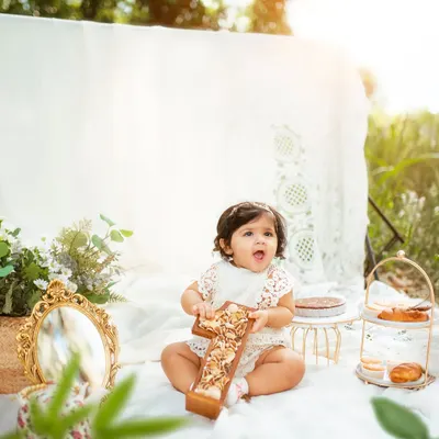 A perfect first birthday picnic. This little girl is holding a wooden "One" prop, surrounded by beautiful decor in the warm afternoon sun.