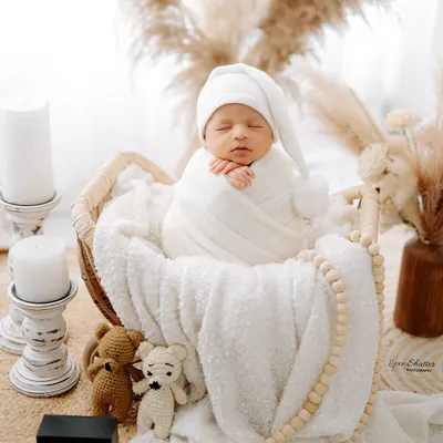 A perfectly swaddled newborn wearing a cute pom-pom hat, sleeping peacefully in a wicker basket. This showcases my classic, neutral-toned setup.