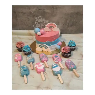 A complete baby shower dessert table set, including a gender-reveal themed cake, matching cupcakes, and adorable custom cakesicles.