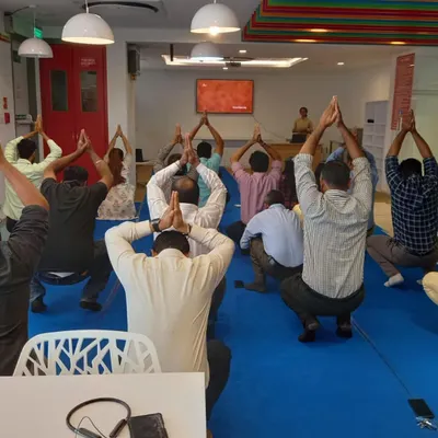 A team practices a simple standing asana during an office wellness workshop. These sessions are designed to be done in work clothes, making it easy to integrate a moment of wellbeing into a busy corporate schedule.