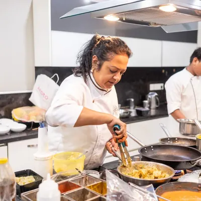 Our co-founder and chef, Sharmistha, in her element, stirring a dish in a busy kitchen during a catering event. This is where the magic begins.