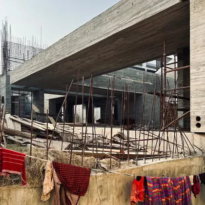 A view of the upcoming villas in Moradabad during construction. The image captures the contrast between the finished, heavy concrete cantilever and the daily life happening around the construction site.
