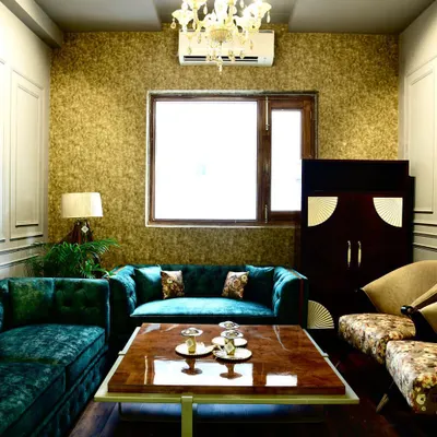 A luxurious living room featuring a deep teal velvet sofa, gold-textured wallpaper, and classic wall moulding. The combination of rich colours and textures creates a warm and inviting atmosphere.