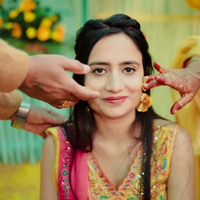 A classic Haldi portrait. We capture the moment the turmeric paste is first applied, focusing on the bride's calm expression and the hands of loved ones blessing her.