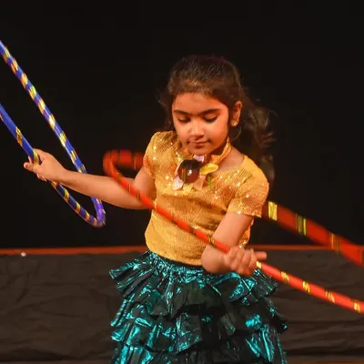 A close-up of one of our young performers skillfully maneuvering multiple hoops during a stage performance. It's a testament to the coordination and focus they build in our classes.