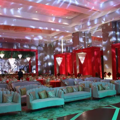 A wide view of a luxurious sangeet hall, decorated in a bold red and gold theme. We arranged elegant lounge seating to create a comfortable yet glamorous atmosphere for guests.