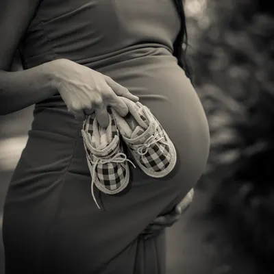 A close-up, artistic shot focusing on the tiny details. These little plaid shoes, held against the bump, tell a big story in classic black and white.
