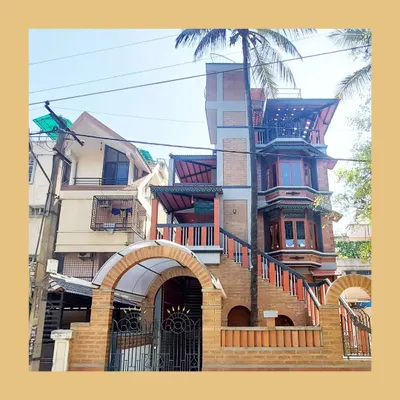 The full facade of the Basavanagudi residence, showcasing a dynamic interplay of materials, from the arched brick entrance to the intricate bay windows and shaded balconies.