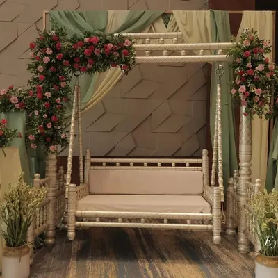 This elegant seating area is perfect for a sophisticated baby shower. A classic white swing is beautifully adorned with arrangements of pink roses and lush greenery, set against soft sage drapes for a serene and picturesque photo spot.