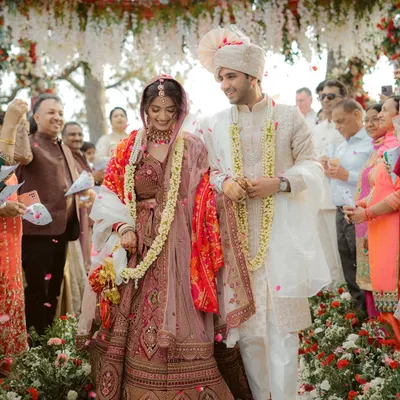 The couple walks together after their jaimala ceremony, surrounded by smiling family and a shower of petals. This captures the joy of a Hindu wedding.