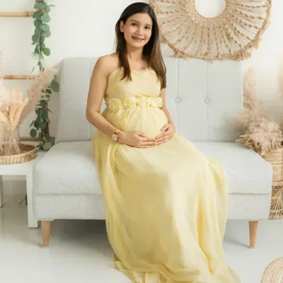Seated comfortably in my bright, boho-chic studio, this mother-to-be radiates serenity in a soft yellow gown. The natural textures of the decor create a warm and inviting atmosphere.