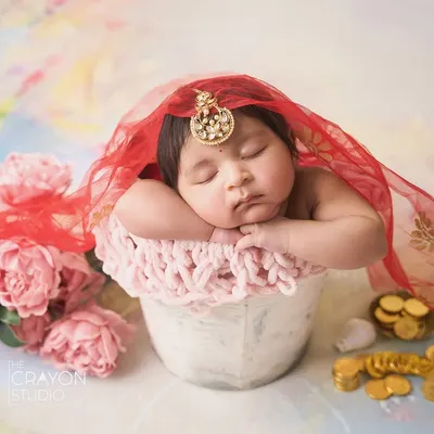 A newborn baby girl dressed in traditional Indian attire, complete with a maang tikka and red veil, sleeping peacefully. This is a beautiful way to honor cultural heritage in a newborn session.