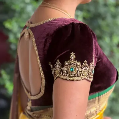 A client showcasing the elegant back cutout and puff sleeves of her deep wine velvet blouse. The gold zardosi embroidery on the sleeve cuff adds a touch of regal splendor.
