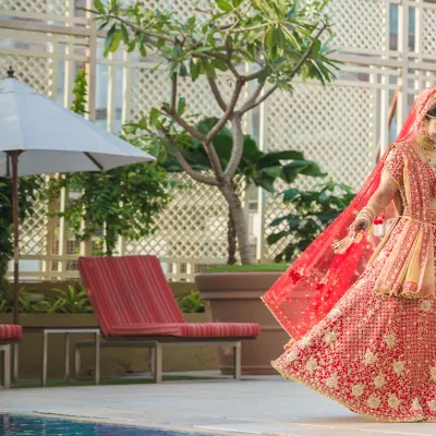 A stunning shot of a bride in a red lehenga walking by the poolside, her veil flowing behind her, creating a sense of movement and grace.
