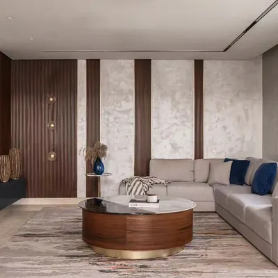 Getting the scale of furniture right is key to a room's flow. In this living room, the large L-shaped sofa defines the seating area without overwhelming it, while the round coffee table adds a contrasting shape and keeps movement easy. The mix of wood, marble, and textured wallpaper creates a layered, sophisticated look.