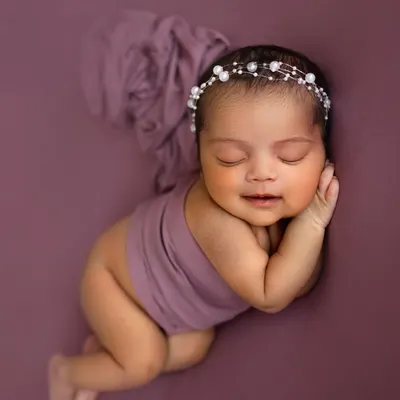 That tiny newborn smile is everything! I love capturing these fleeting moments. This little one is posed so peacefully on a simple purple backdrop, making her the star of the show.
