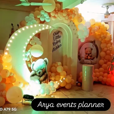 A dreamy naming ceremony decoration featuring a light-up crescent moon, a sleeping teddy bear prop, and a warm-toned balloon arch for "Our Little Baby Mishka".