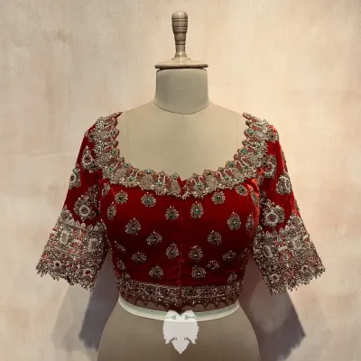 A royal red velvet blouse for bride Bhavana, featuring a neckline designed to resemble jewelry, embellished with kundan, pearls, and beads.