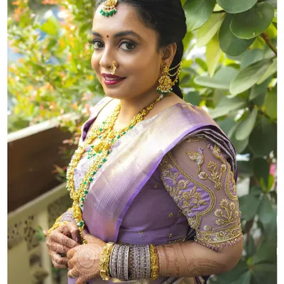 A beautiful portrait of a bride on her wedding day, dressed in a lavender silk saree with intricate gold embroidery. Her happy expression and traditional attire perfectly capture the joy of the celebration.