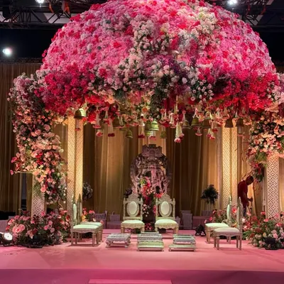A frontal view of the spectacular 'Gulabi Shaam' mandap, showcasing the sheer density of pink and white florals that form the dome. The design is anchored by a backdrop featuring a Shreenathji idol, blending opulence with divine blessings for the wedding ceremony.