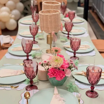 A top-down view of the Parisian baby shower tablescape, showing the harmony between the sage green plates, pink floral arrangements, and gold cutlery.