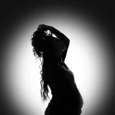 A stunning silhouette portrait of a mother to be. The backlighting creates a beautiful halo effect, highlighting her form and capturing a moment of quiet strength and beauty.