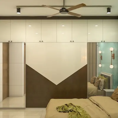 A modern bedroom featuring a custom wardrobe with a unique diagonal two-tone finish on the sliding doors. The design includes mirrored panels and is complemented by stylish wall-mounted lights.