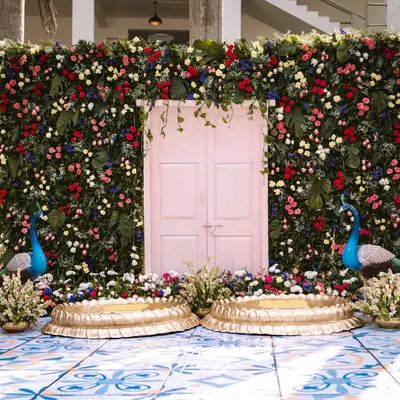 A tropical Haldi dream. We created a stunning backdrop with a wall of fresh green leaves, a pink door, and vibrant florals, complete with peacock and flamingo props for a fun, exotic touch.