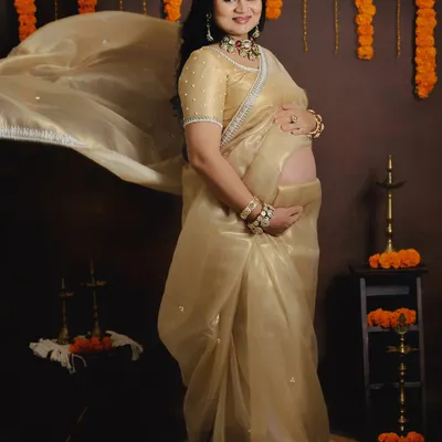 A breathtaking solo portrait in a golden organza saree. The fabric toss adds a sense of movement and grace, while the traditional decor with marigold garlands completes the culturally rich aesthetic.