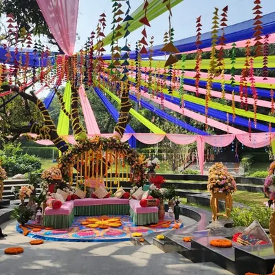 A spectacular Mehendi setup in Jim Corbett, featuring a canopy of colorful drapes over a multi-tiered seating area, creating a festival-like atmosphere.