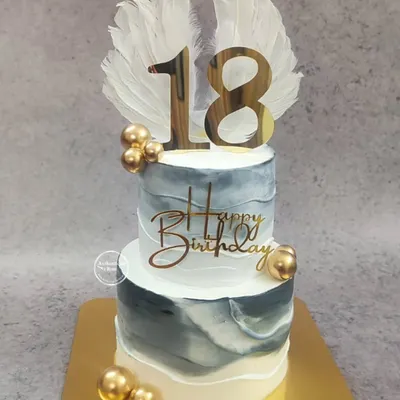 An angelic two-tiered cake for an 18th birthday. The design features a marble effect in grey and white, accented with gold spheres and topped with beautiful white angel wings.