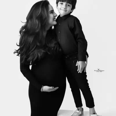 A beautiful black and white portrait of a mother and her son. The clean, high-key background puts all the focus on their loving interaction and the mom's glowing pregnancy.