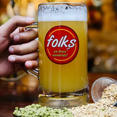 A classic shot for Folks brewpub. The branded mug is front and center, with raw ingredients like hops and barley scattered around to emphasize the 'craft' nature of the beer.