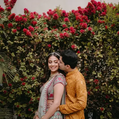 A sweet, candid moment between the couple at their Mehendi in Jaipur. The bride's makeup is fresh and radiant, with a soft pink lip that complements the floral embroidery on her Anita Dongre lehenga.
