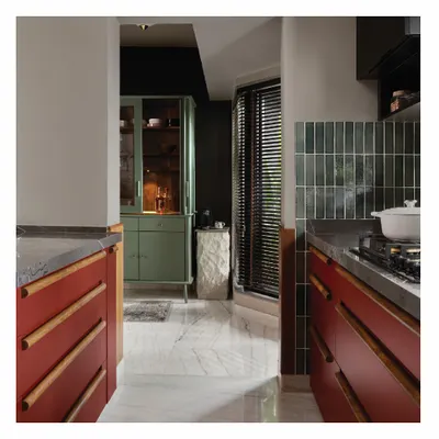 This is my personal kitchen, my solace. I designed it with bold Marsala Red cabinets and custom wooden handles. The standalone sage green bar cabinet and stone pedestal for the coffee machine create a functional and colorful 'Cook and Drink' unit.